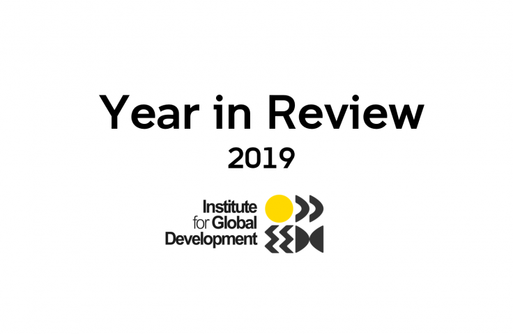 The text reads: Year in Review 2019 by The Institute for Global Development. The Institute for Global Development visual identity sits below that as a 2 x 2 grid. In clockwise: a yellow circle, two boomerangs facing forward, two chevrons and two half moons facing inwards.