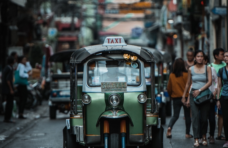 A tuk tuk (peddi cab) is heading towards the camera down a street.